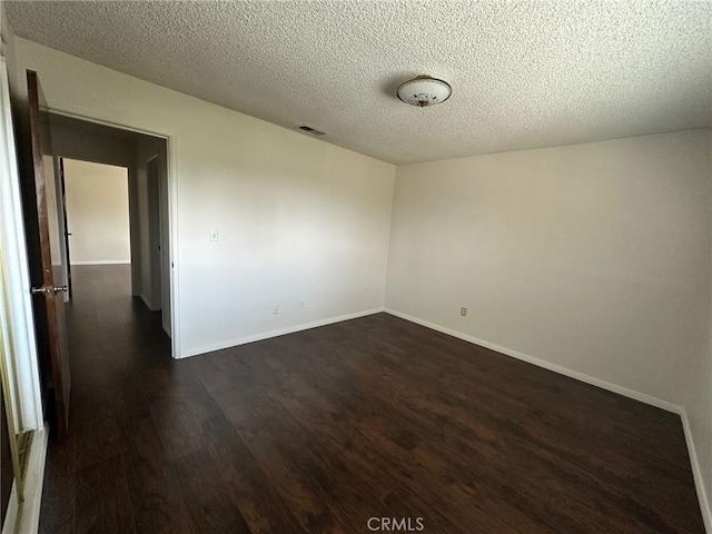 unfurnished room featuring a textured ceiling, dark wood finished floors, visible vents, and baseboards