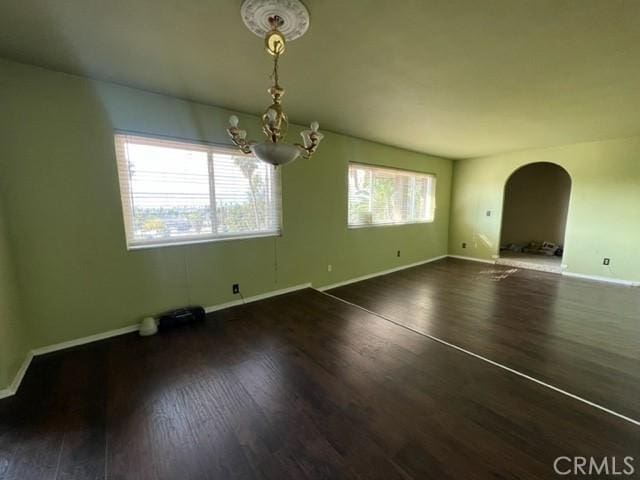 unfurnished dining area featuring arched walkways, dark wood-style flooring, plenty of natural light, and baseboards