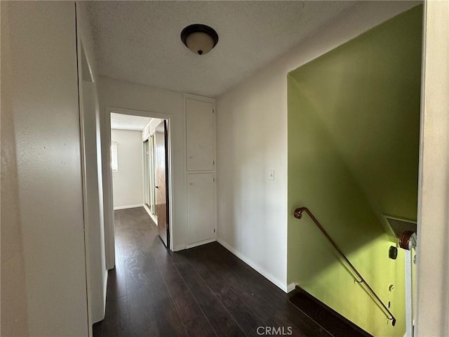 corridor featuring baseboards, dark wood finished floors, a textured ceiling, and an upstairs landing