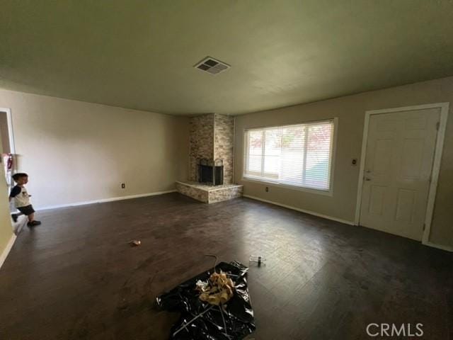 unfurnished living room with baseboards, visible vents, and a stone fireplace