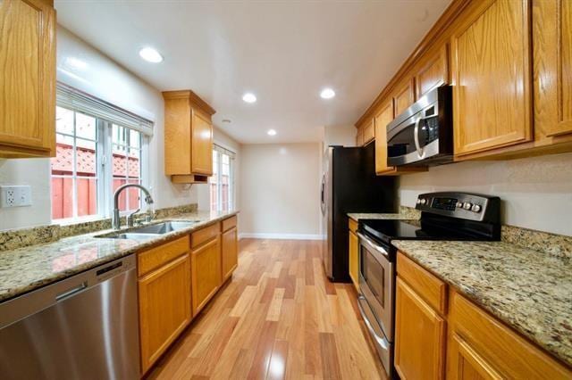 kitchen featuring light hardwood / wood-style floors, light stone counters, stainless steel appliances, and sink