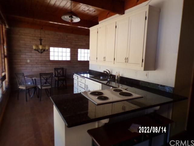 13425 Jensen Rd, Clearlake Oaks, CA 95423 - kitchen featuring kitchen peninsula, white cabinetry, a notable chandelier, brick wall, and pendant lighting