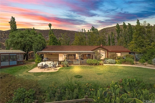 back house at dusk featuring a patio area, a yard, and a mountain view