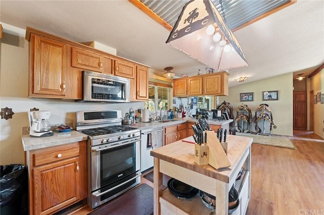 kitchen featuring appliances with stainless steel finishes, tile counters, light hardwood / wood-style flooring, sink, and vaulted ceiling