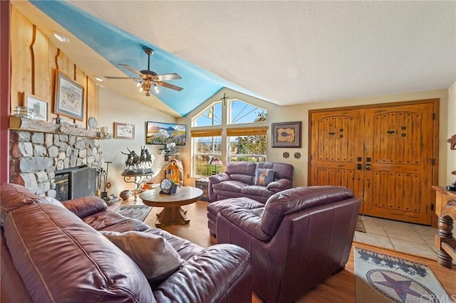 living room featuring a stone fireplace, light tile floors, a textured ceiling, ceiling fan, and lofted ceiling