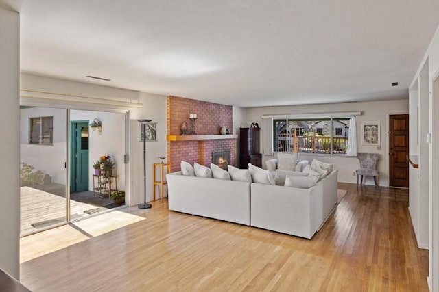 living room featuring brick wall, a brick fireplace, and light wood-type flooring