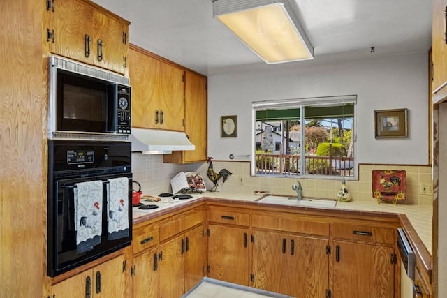 kitchen featuring tile countertops, tasteful backsplash, black appliances, and sink