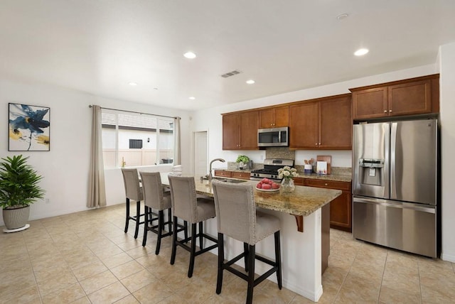 kitchen with stainless steel appliances, a kitchen bar, a center island with sink, light stone counters, and sink