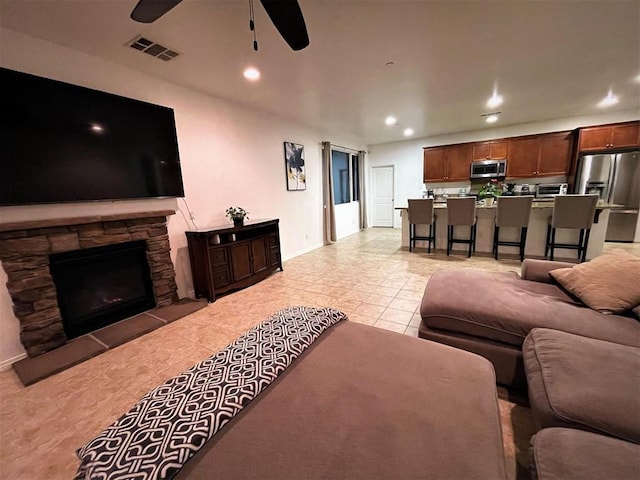 tiled living room with a stone fireplace and ceiling fan