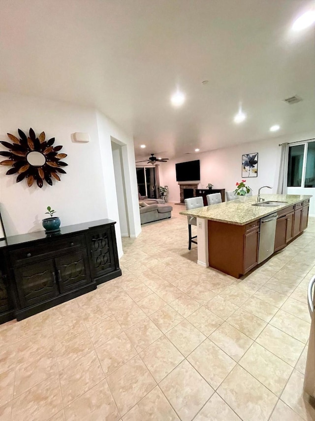 kitchen featuring an island with sink, ceiling fan, sink, light stone counters, and dishwasher