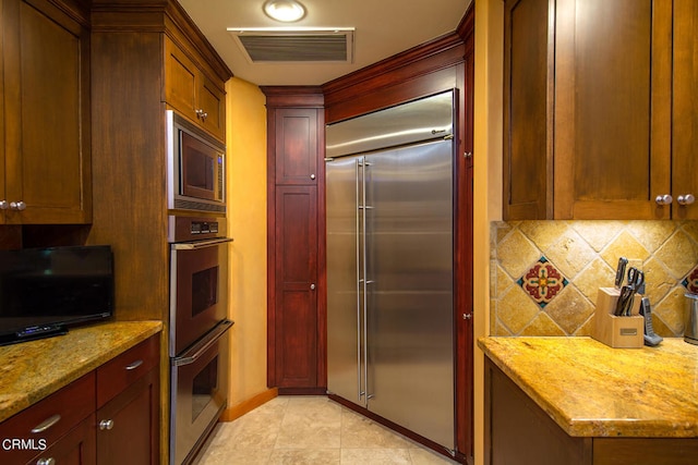 kitchen featuring backsplash, light stone counters, built in appliances, and light tile floors