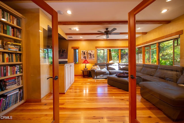 living room featuring beam ceiling, ceiling fan, built in shelves, and light wood-type flooring