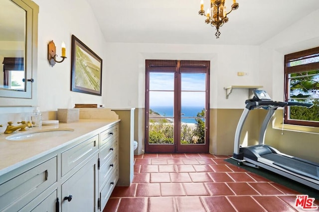 workout room featuring an inviting chandelier, dark tile flooring, sink, and a water view