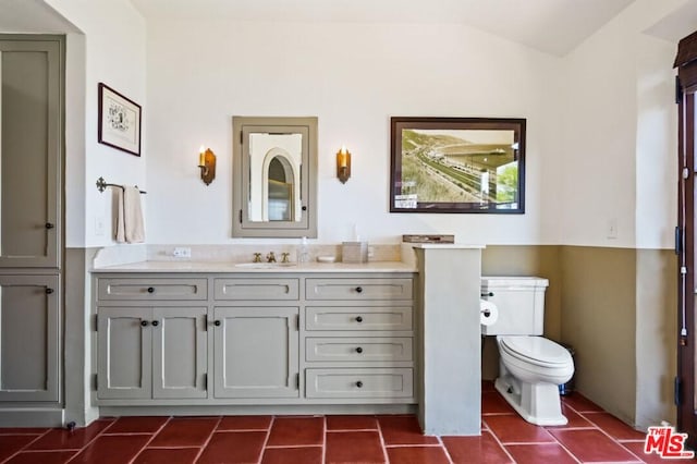 bathroom with toilet, tile flooring, vanity, and lofted ceiling