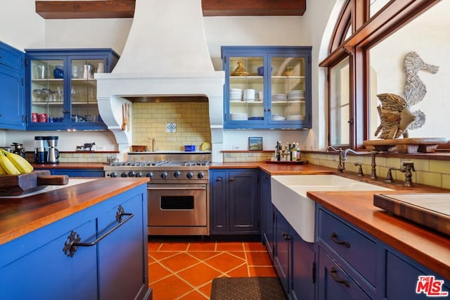 kitchen featuring dark tile floors, blue cabinets, premium range hood, designer range, and tasteful backsplash