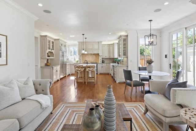 living room with an inviting chandelier, sink, hardwood / wood-style floors, and crown molding