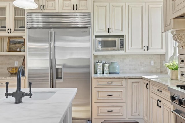 kitchen with cream cabinetry, tasteful backsplash, light stone countertops, stainless steel appliances, and sink