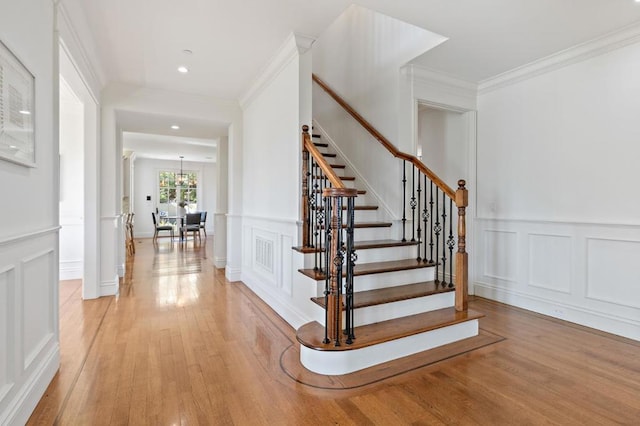 stairway featuring wood-type flooring, a chandelier, and crown molding