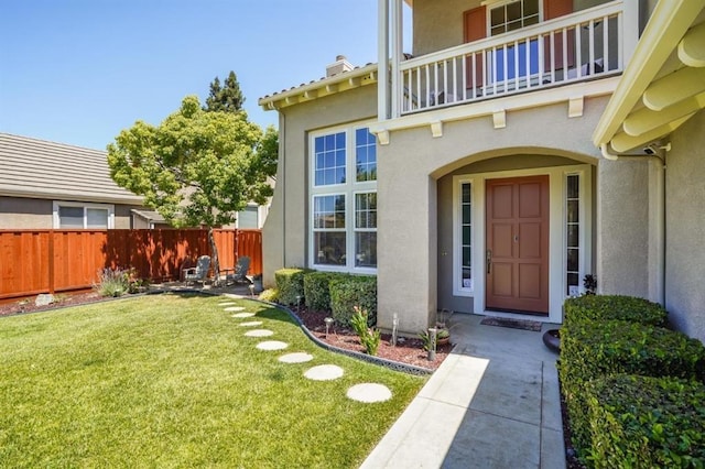 view of exterior entry with a balcony and a lawn