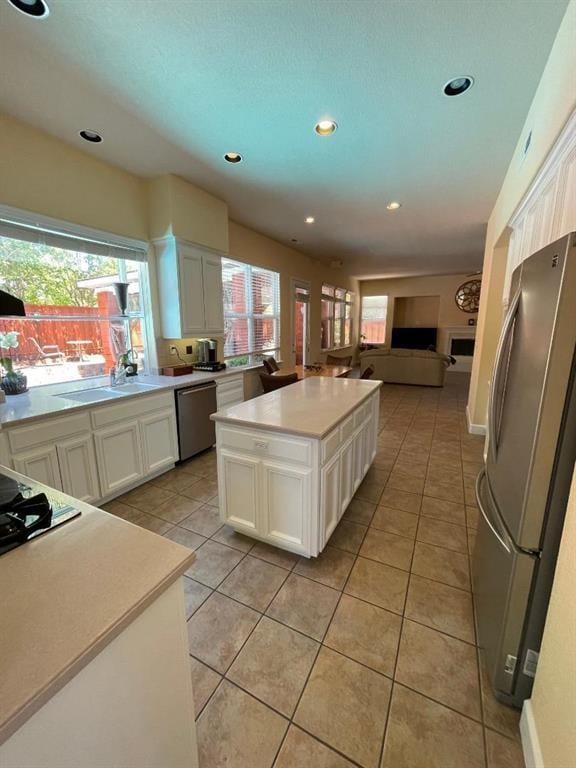 kitchen featuring light tile floors, stainless steel appliances, a kitchen island, and white cabinetry