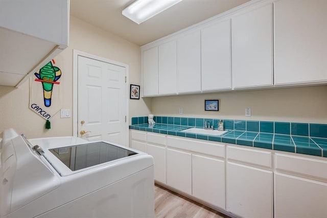 laundry area featuring cabinets, washer and dryer, sink, and light hardwood / wood-style flooring