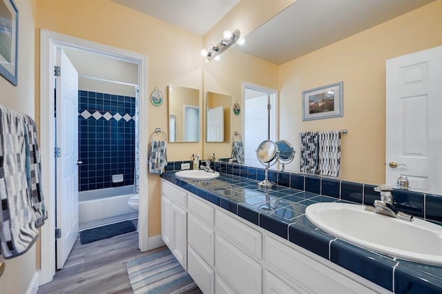 full bathroom with hardwood / wood-style floors, double vanity, toilet, and tiled shower / bath