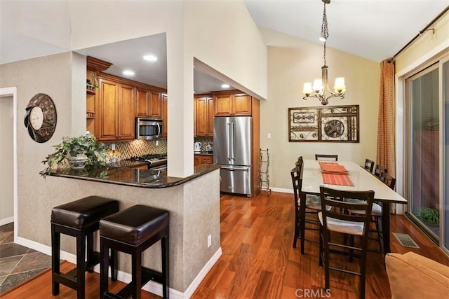 kitchen with a chandelier, kitchen peninsula, tasteful backsplash, appliances with stainless steel finishes, and hanging light fixtures