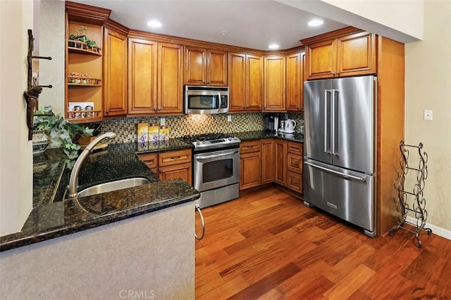 kitchen featuring stainless steel appliances, dark stone counters, backsplash, dark hardwood / wood-style floors, and sink