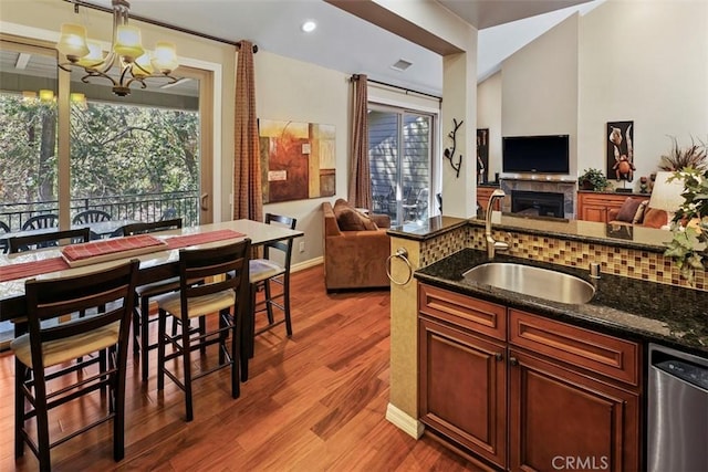 kitchen with decorative light fixtures, dark wood-type flooring, dark stone countertops, a notable chandelier, and dishwasher