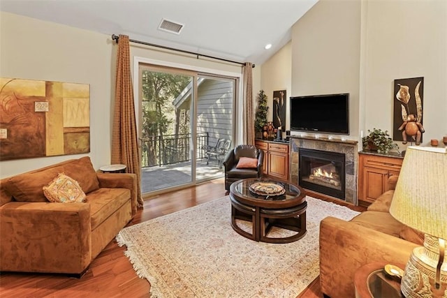 living room featuring lofted ceiling, wood-type flooring, and a tile fireplace