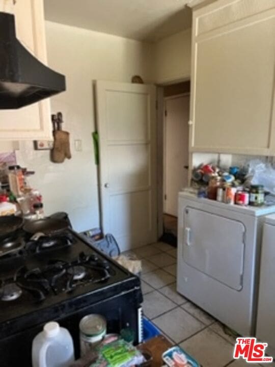 kitchen featuring light tile patterned floors, black range with gas cooktop, white cabinetry, washer / clothes dryer, and range hood