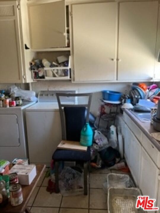 clothes washing area featuring cabinets, tile patterned flooring, and washing machine and dryer