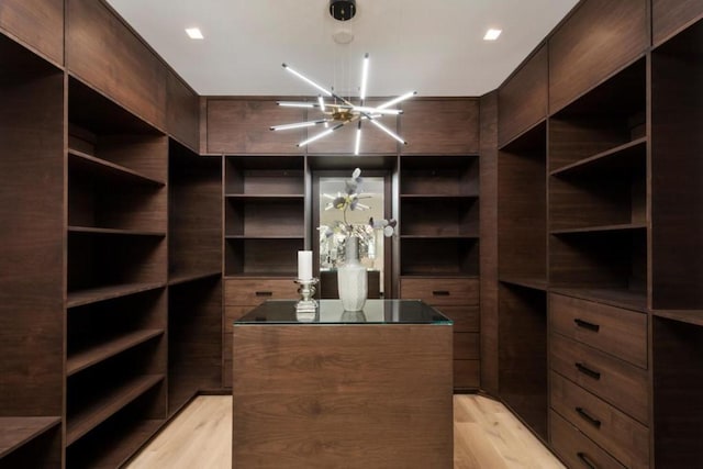 spacious closet with light hardwood / wood-style flooring and a notable chandelier