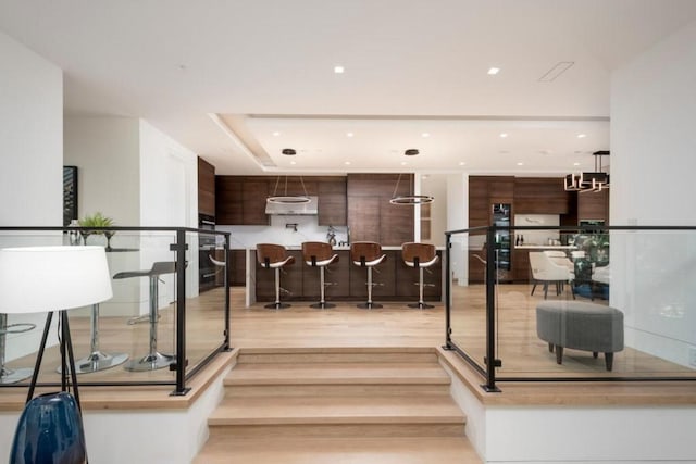 kitchen featuring a chandelier, a kitchen island, a breakfast bar, dark brown cabinets, and light wood-type flooring