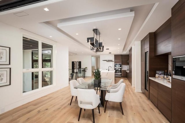 dining space featuring a tray ceiling, light hardwood / wood-style floors, and sink