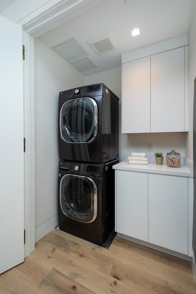 clothes washing area with stacked washing maching and dryer, cabinets, and light wood-type flooring