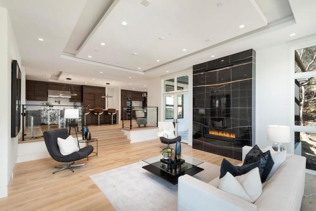 living room with a tiled fireplace, a tray ceiling, and plenty of natural light