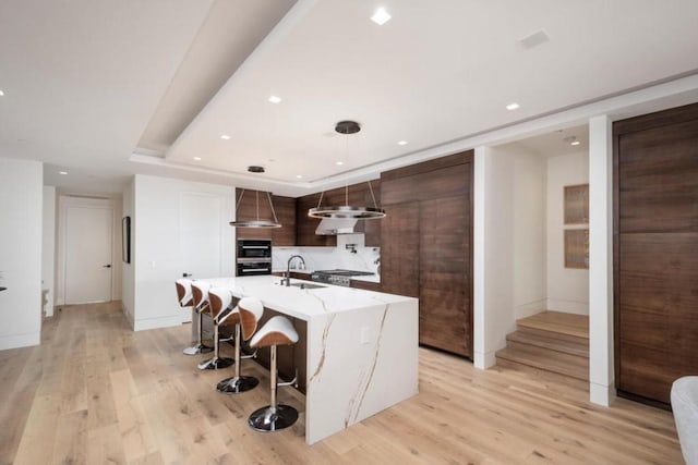 kitchen featuring a kitchen breakfast bar, light hardwood / wood-style floors, sink, a center island with sink, and dark brown cabinets