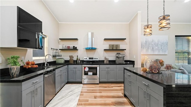 kitchen with gray cabinetry, sink, wall chimney range hood, light hardwood / wood-style flooring, and appliances with stainless steel finishes