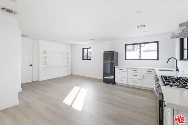 kitchen with stainless steel gas range, sink, black refrigerator, white cabinetry, and light wood-type flooring