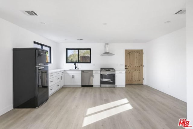 kitchen with white cabinets, light wood-type flooring, stainless steel appliances, and wall chimney exhaust hood