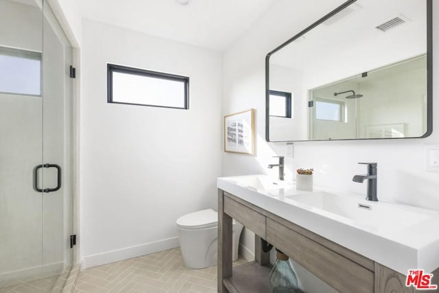 bathroom featuring toilet, vanity, a shower with door, and a wealth of natural light