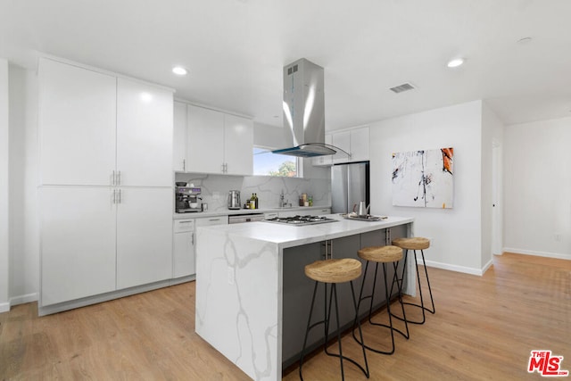 kitchen featuring white cabinetry, a kitchen breakfast bar, light hardwood / wood-style floors, stainless steel appliances, and island range hood