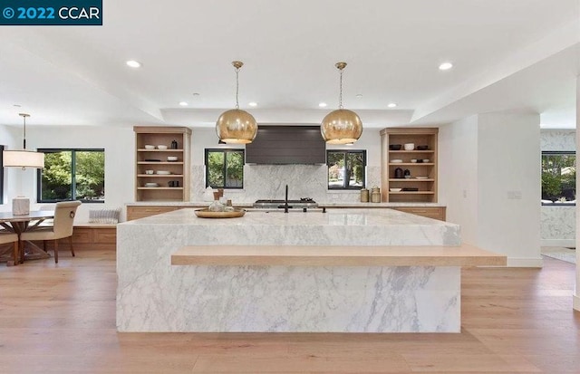 kitchen with light hardwood / wood-style flooring, an island with sink, custom range hood, and plenty of natural light