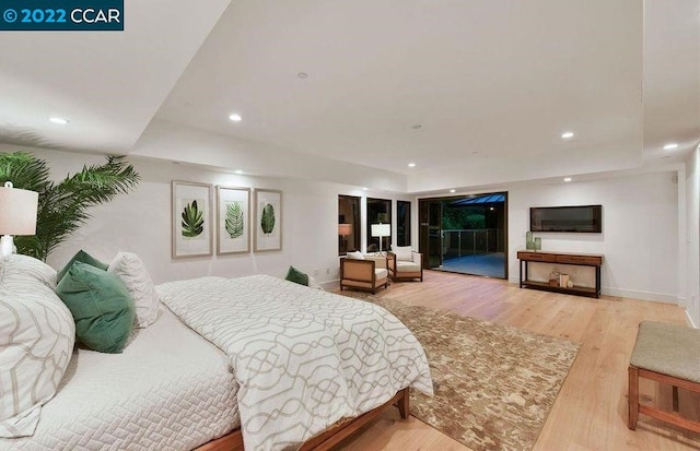 bedroom featuring a raised ceiling, access to exterior, and light wood-type flooring