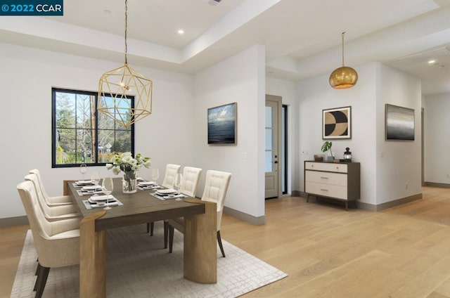 dining space featuring a chandelier, light wood-type flooring, and a tray ceiling