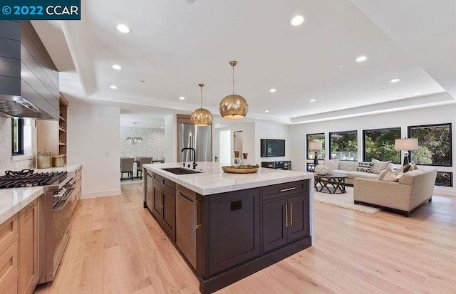 kitchen featuring custom exhaust hood, gas range, hanging light fixtures, light wood-type flooring, and sink