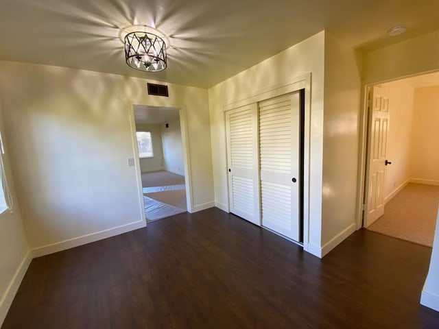 unfurnished bedroom featuring a closet, a notable chandelier, and dark wood-type flooring