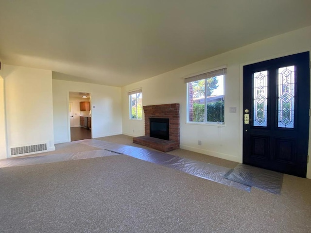 unfurnished living room with a brick fireplace and dark colored carpet