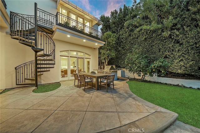 patio terrace at dusk featuring a balcony, french doors, and a yard